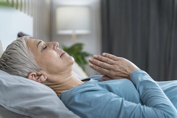 kvinna som utövar meditation för sömn, liggandes i sängen precis innan hon ska sova