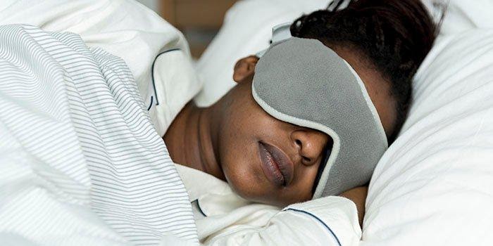 vrouw die gezichtsmasker gebruikt voor een goede nachtrust en de 7-8 uur slaap krijgt die een volwassene nodig heeft