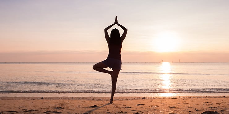 mujer de pie en una clase de yoga realizando la postura del árbol Vrikshasana en la playa