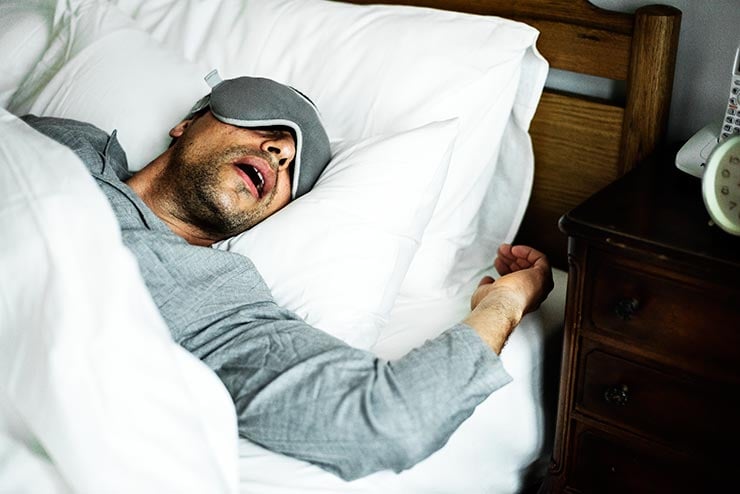 Mann benutzt eine Schlafmaske, um sicherzustellen, dass er einschläft und die ganze Nacht durchschlafen kann