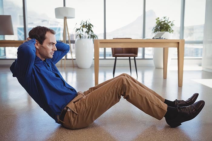 determined executive preforming crunches at work as part of workplace wellness