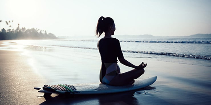 chica sentada en postura de meditación sobre una tabla de surf practicando cómo despejar la mente
