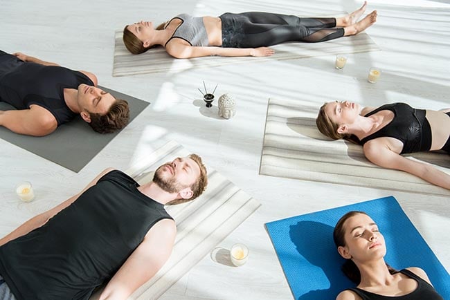 öt fiatal személy meditál holttest pózban a jóga nidra gyakorlása közben