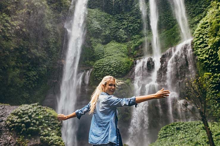 Frau hält an, um bei einem Spaziergang einen Wasserfall im Wald zu genießen