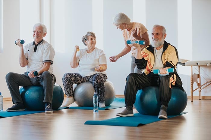 группа пожилых людей выполняет упражнение пилатес