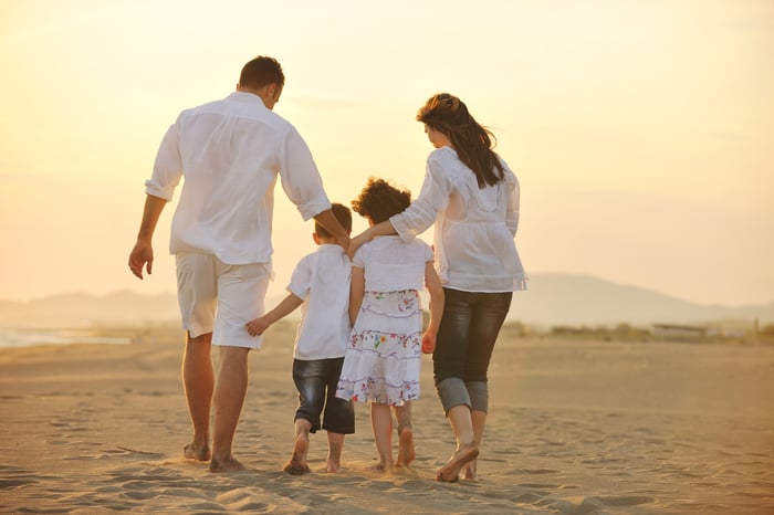 Familj, två vuxna och två barn, som går tillsammans längs stranden
