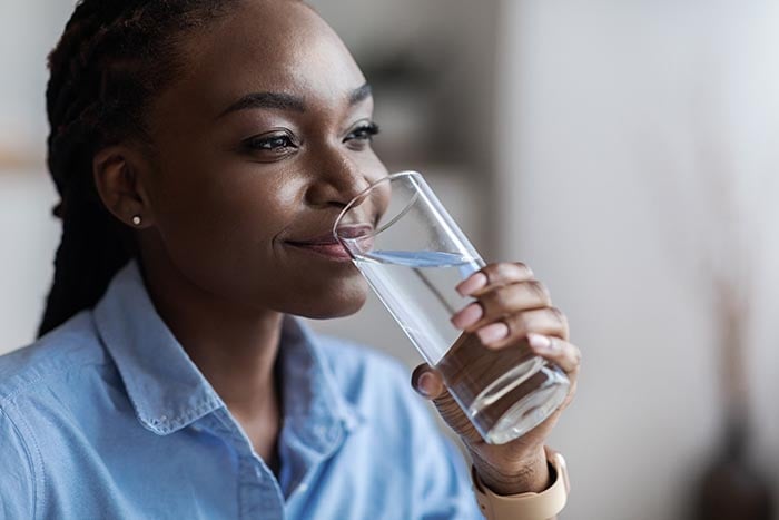 eine Frau, die Mineralwasser trinkt, um eine ausreichende Flüssigkeitszufuhr zu gewährleisten