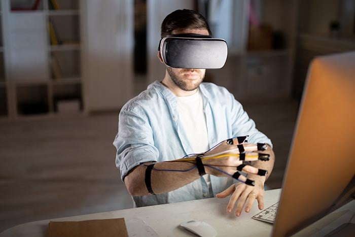 Uomo che lavora da casa usando la sua scrivania come spazio di lavoro virtuale, utilizzando un'attrezzatura per la realtà virtuale