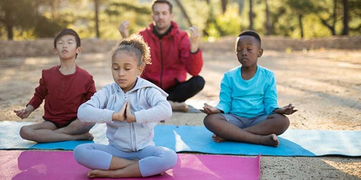 coach and children doing meditation for kids in the park