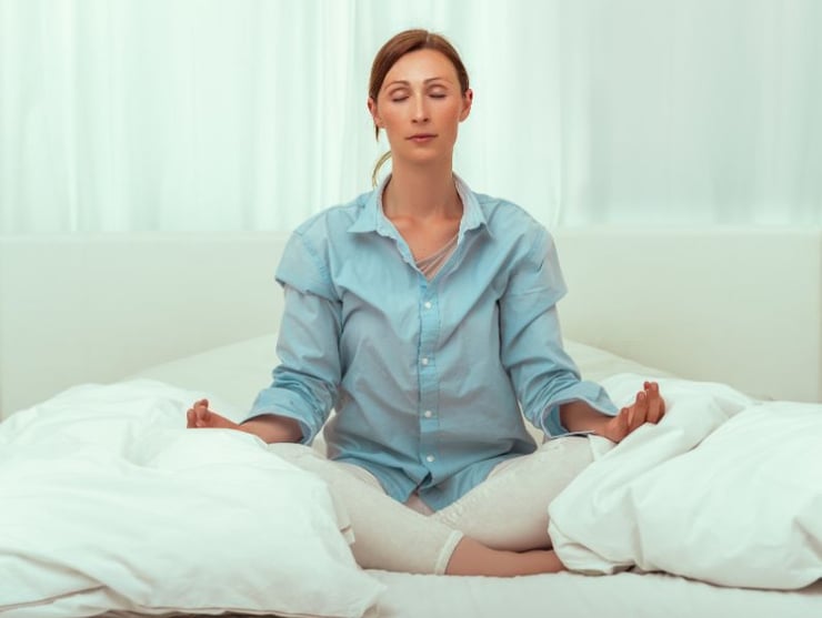 kvinna som sitter i sänger och mediterar för att nollställa hjärnan för mental klarhet