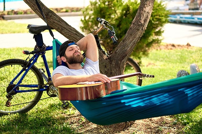 en man som sover utomhus i en hammock hållandes i en gitarr