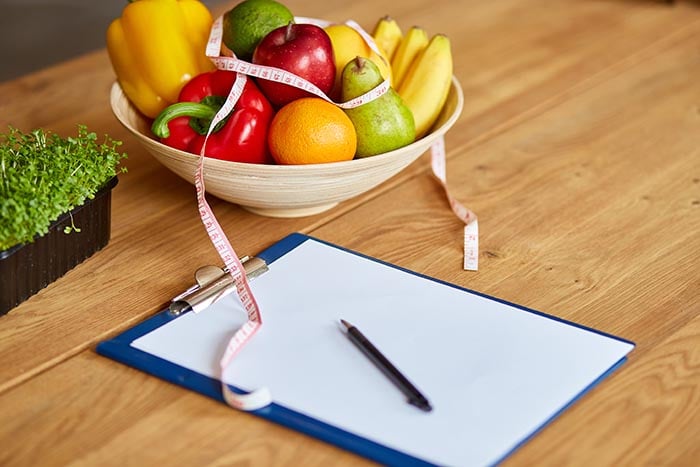 en skål fylld med hälsosam kost, penna och papper, för att notera ens matvanor på jobbet