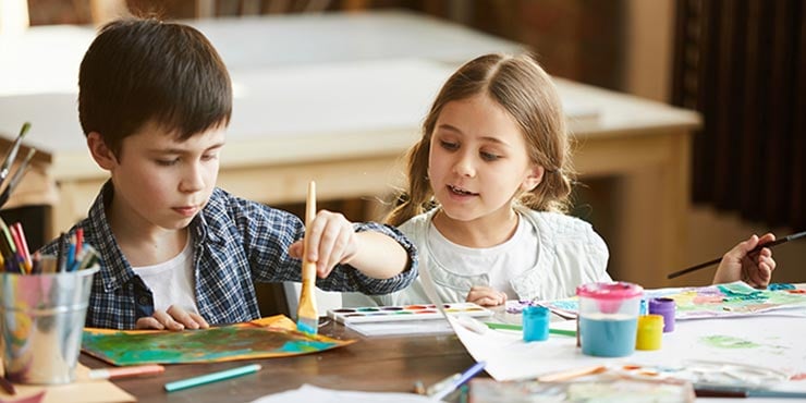 to børn sidder ved et bord og maler sammen