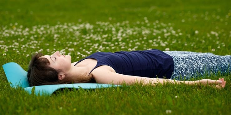 kvinna som gör yoga nidra liggande i savasana-ställning