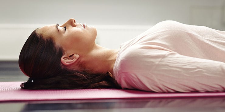 Frau liegt auf einer Yogamatte und entspannt ihre Muskeln bei einer Schlafmeditation