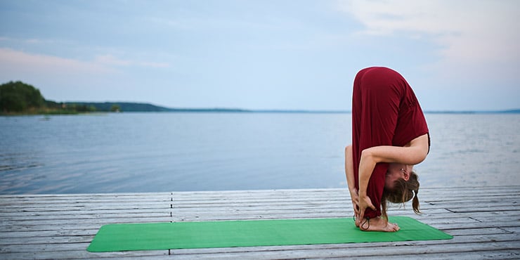 woman performing padhastasana standing outside next to the water