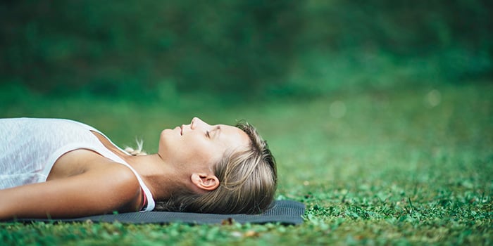 femeie practicând yoga poziția cadavrului în aer liber bucurându-se de beneficiile yoga nidra