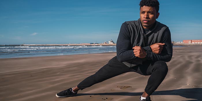 man som tränar yoga på stranden för att minska skaderisken vid löpning