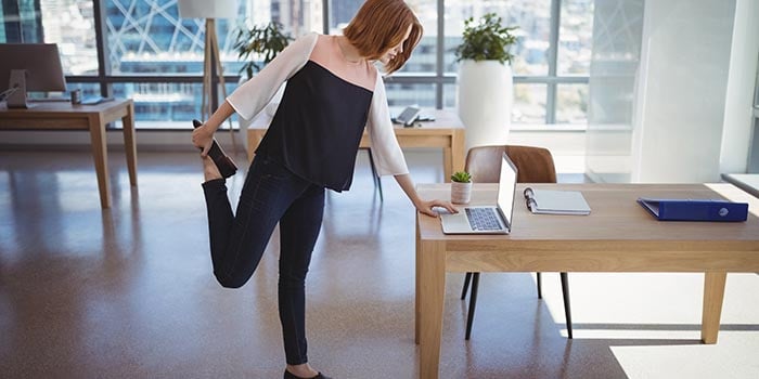 kvinna som står och stretchar på jobbet samtidigt som hon arbetar på sin dator