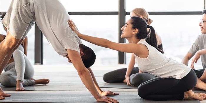 female coach correcting hatha yoga beginner at group class