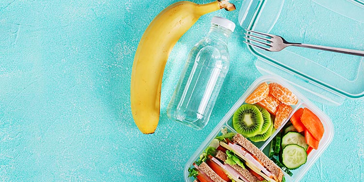 Fiambrera escolar de hábitos saludables con sándwich de verduras, agua y un plátano.