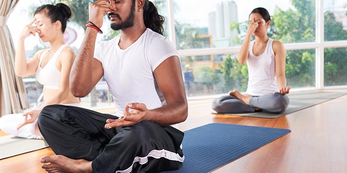 man and woman doing alternate nostril breathing in a yoga studio