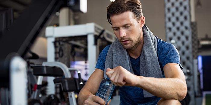 man with water bottle at gym drinking water to ensure proper healthy hydration