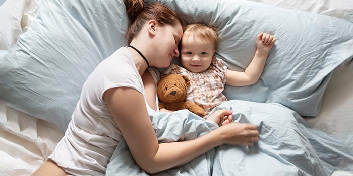 Mutter im Schlafanzug mit schlafendem Baby übt sich in gesunder Schlafhygiene