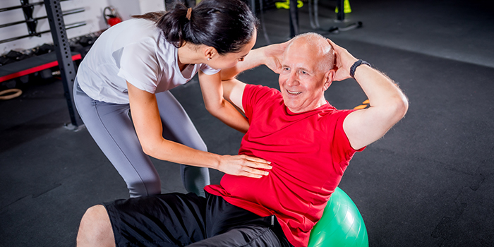 En äldre man som utövar pilates med hjälp av en pilates tränare