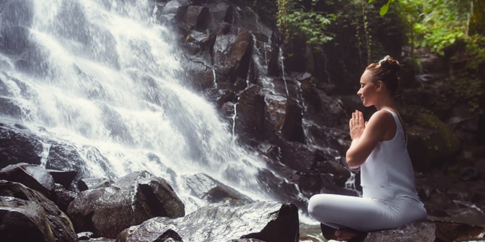 kvinna som sitter på en sten, utövar yoga framför ett vattenfall