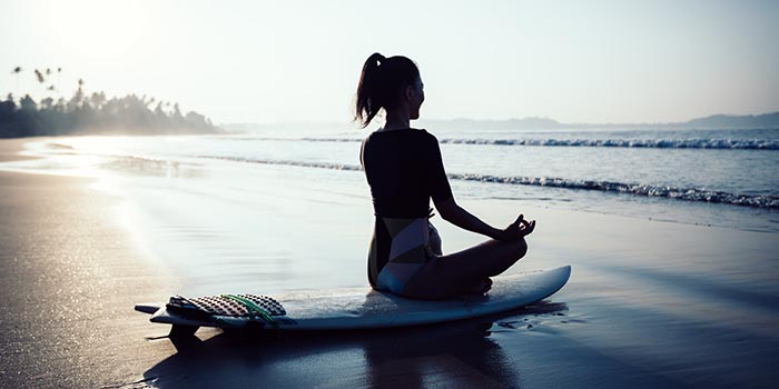 En kvinna som sitter på en surfbräda på stranden för att få en lugn stund och en mental nollställning