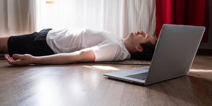 young man with laptop meditating on floor practicing yoga nidra