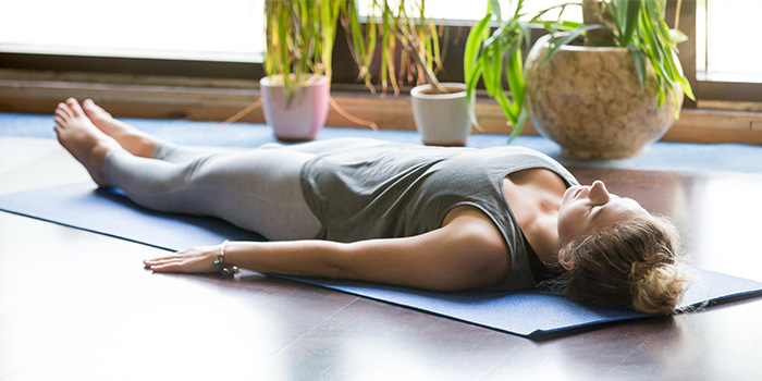 ผู้หญิงทำโยคะที่บ้านท่า Shavasana เป็นส่วนหนึ่งของโยคะนิทรา-700