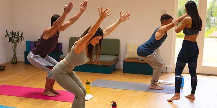 chair pose utkatasana female instructor assisting in group yoga