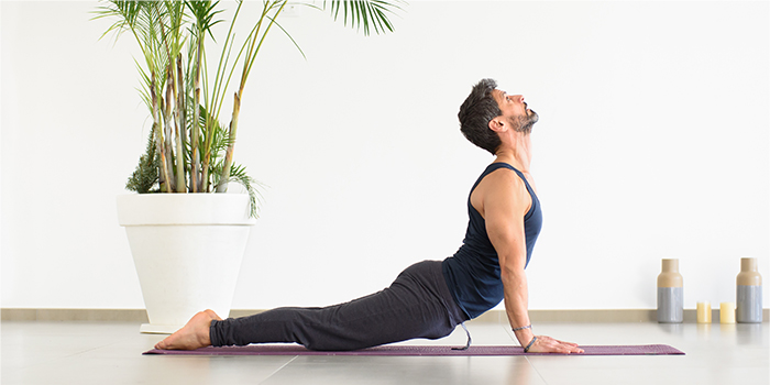Man som utövar vinayasa yoga och gör Upward-facing dog pose på en matta, inomhus