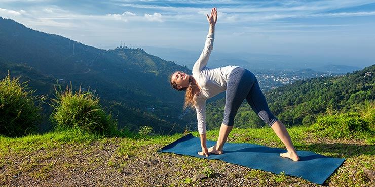 woman performing parivrtta trikonasana, revolved triangle pose outdoors
