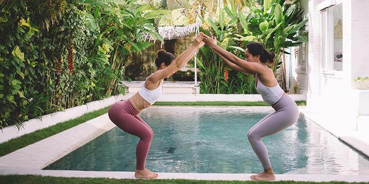 two women doing utkatasana or chair pose by the pool